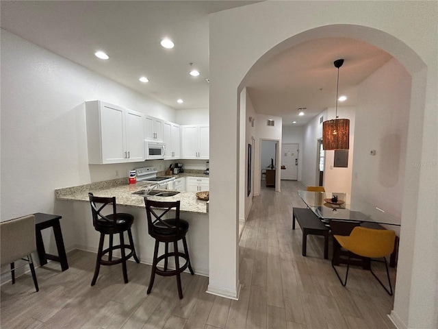 kitchen featuring white appliances, kitchen peninsula, pendant lighting, white cabinets, and light hardwood / wood-style flooring