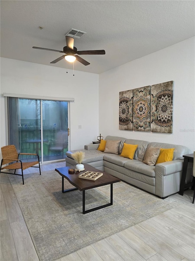 living room with a textured ceiling, light wood-type flooring, and ceiling fan