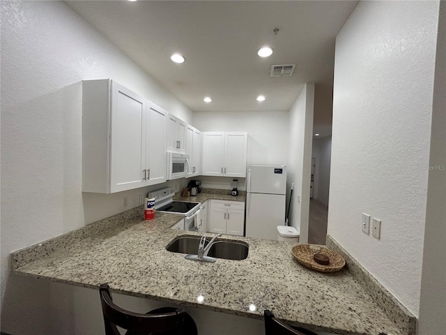 kitchen with white appliances, light stone countertops, kitchen peninsula, and white cabinets