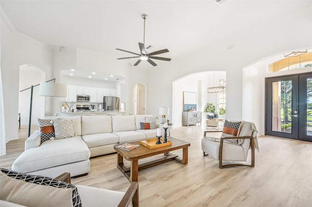 living room with ceiling fan with notable chandelier, crown molding, light hardwood / wood-style floors, and french doors