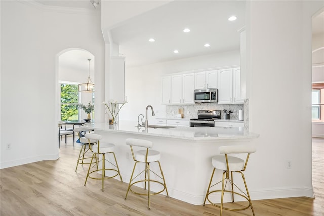 kitchen featuring a kitchen breakfast bar, light hardwood / wood-style flooring, white cabinetry, appliances with stainless steel finishes, and kitchen peninsula