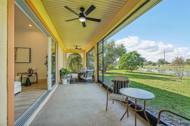 sunroom featuring ceiling fan and a water view