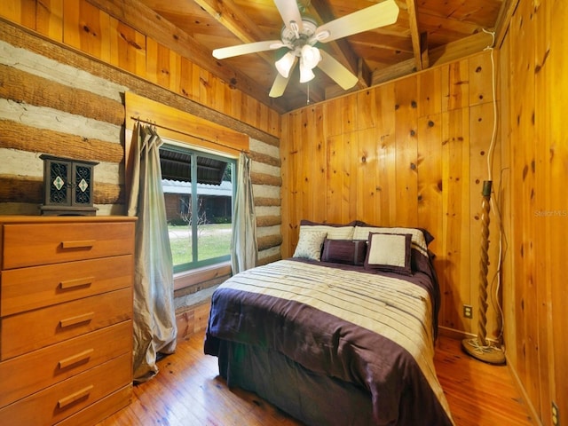 bedroom with ceiling fan, hardwood / wood-style flooring, beamed ceiling, and wooden walls