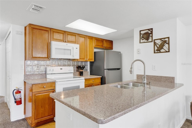 kitchen with kitchen peninsula, light stone countertops, sink, and white appliances