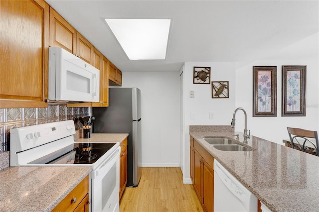 kitchen featuring tasteful backsplash, light stone countertops, light hardwood / wood-style flooring, sink, and white appliances