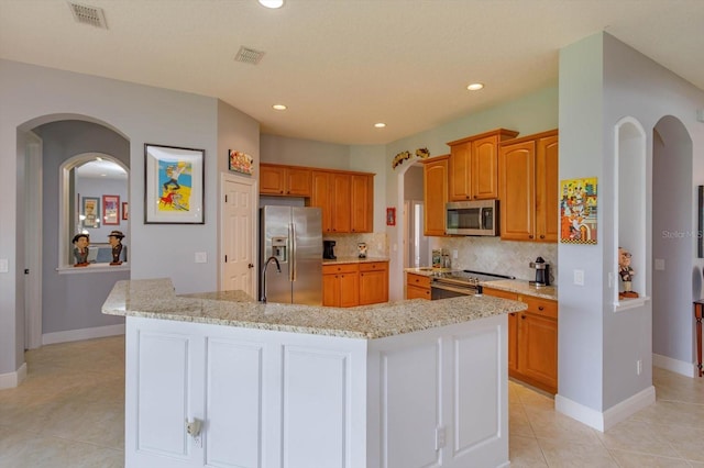 kitchen with tasteful backsplash, appliances with stainless steel finishes, light tile patterned flooring, and an island with sink