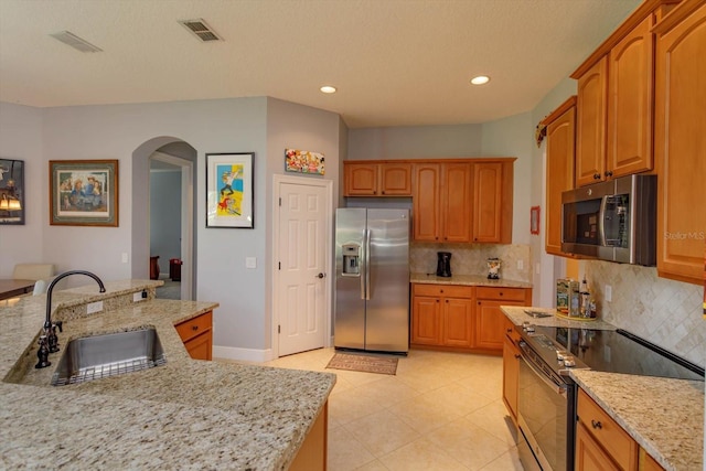 kitchen with decorative backsplash, sink, light stone countertops, light tile patterned floors, and appliances with stainless steel finishes