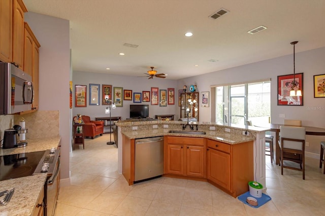 kitchen featuring ceiling fan, appliances with stainless steel finishes, light stone countertops, sink, and decorative light fixtures