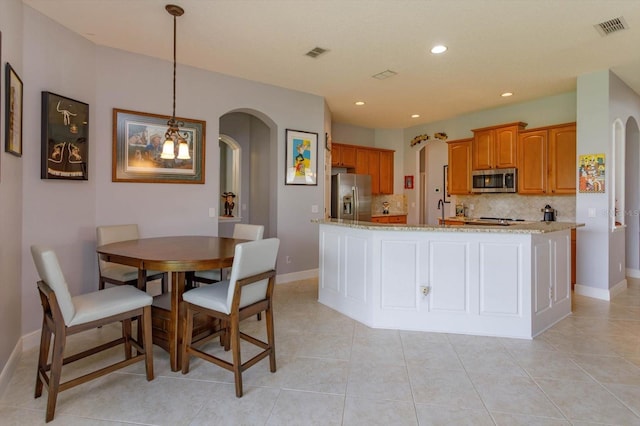 kitchen with hanging light fixtures, light tile patterned floors, backsplash, light stone countertops, and stainless steel appliances