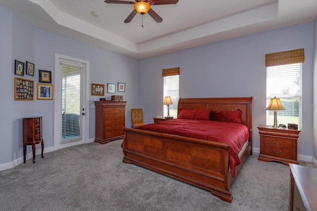 bedroom featuring ceiling fan, multiple windows, a tray ceiling, and access to exterior