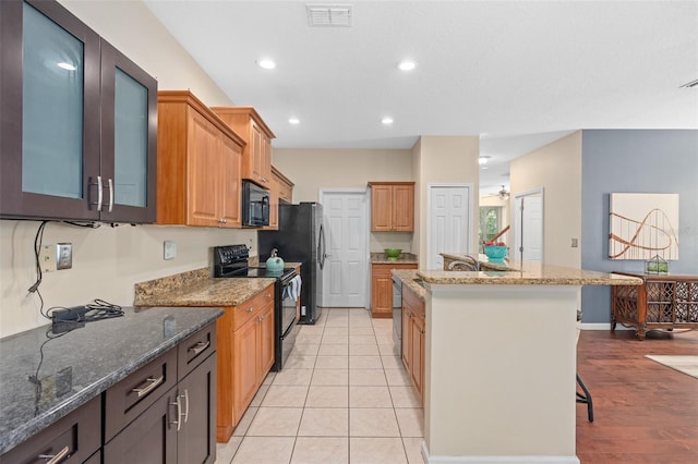 kitchen with light stone counters, black appliances, an island with sink, and a kitchen breakfast bar