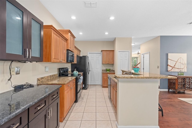 kitchen with stone countertops, black appliances, a kitchen breakfast bar, and visible vents
