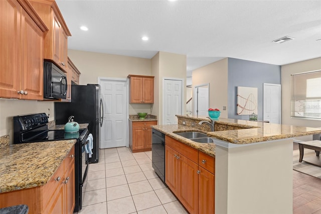 kitchen featuring black appliances, sink, an island with sink, light wood-type flooring, and light stone counters