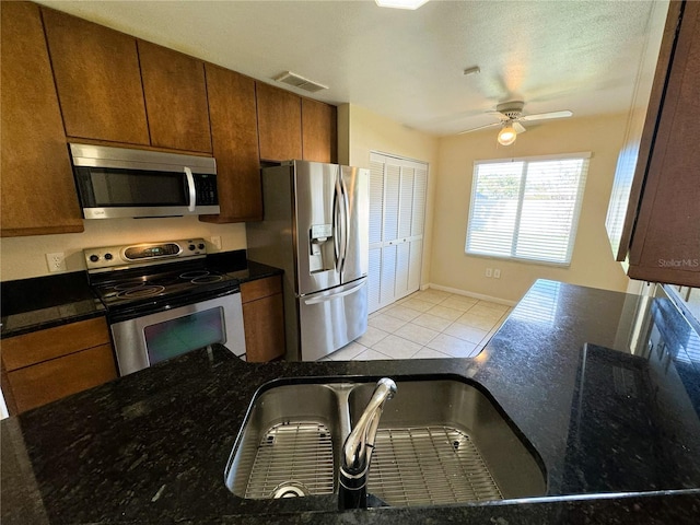 kitchen with appliances with stainless steel finishes, dark stone countertops, light tile patterned flooring, and ceiling fan