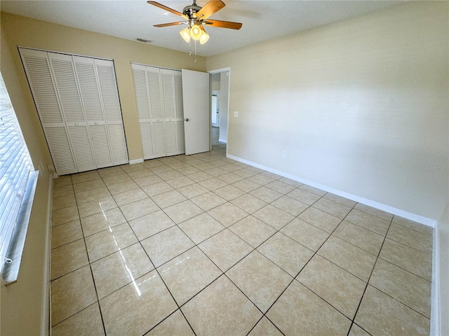 unfurnished bedroom with ceiling fan, multiple closets, and light tile patterned flooring