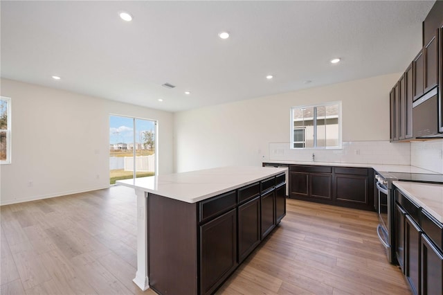 kitchen featuring dark brown cabinetry, stainless steel range with electric stovetop, a center island, light wood-type flooring, and decorative backsplash