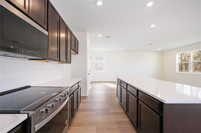 kitchen with backsplash, dark brown cabinetry, stainless steel appliances, and light wood-type flooring