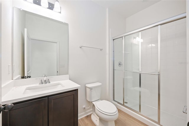 bathroom featuring wood-type flooring, toilet, a shower with door, and vanity