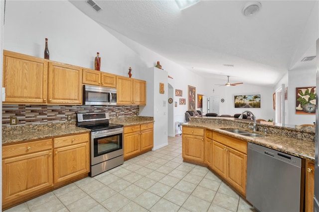 kitchen featuring backsplash, dark stone countertops, sink, vaulted ceiling, and appliances with stainless steel finishes