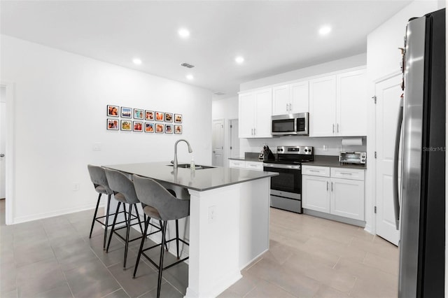 kitchen featuring stainless steel appliances, a center island with sink, sink, a breakfast bar, and white cabinets