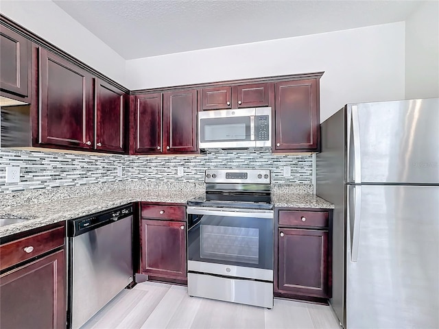 kitchen featuring light hardwood / wood-style floors, stainless steel appliances, light stone countertops, and decorative backsplash