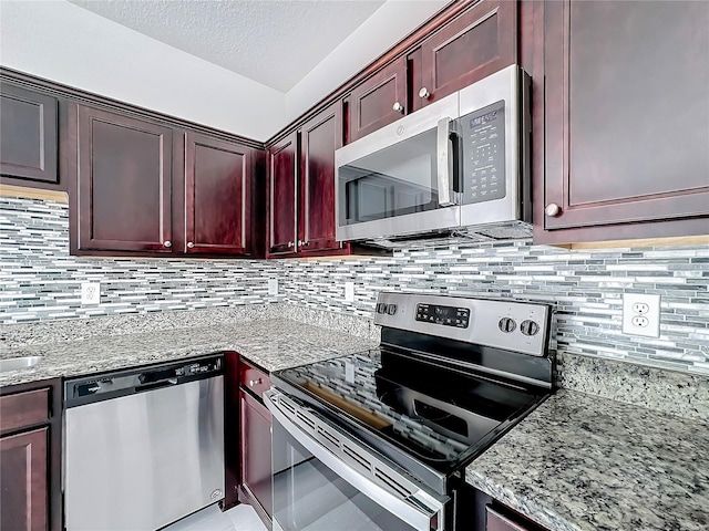 kitchen with appliances with stainless steel finishes, a textured ceiling, light stone countertops, and backsplash