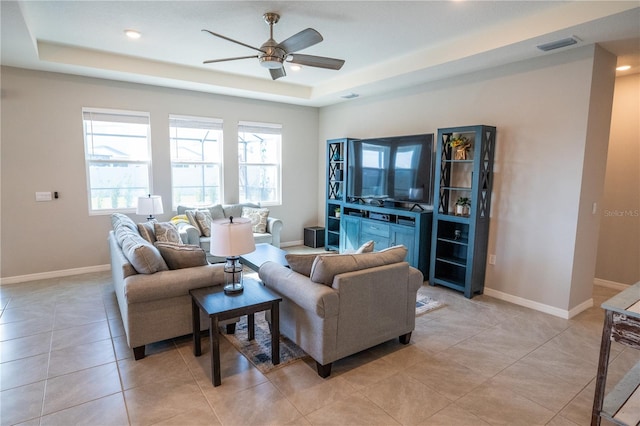 living area featuring light tile patterned floors, ceiling fan, visible vents, baseboards, and a tray ceiling