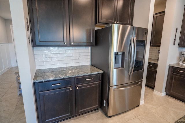 kitchen featuring light tile patterned floors, stone countertops, dark brown cabinetry, stainless steel refrigerator with ice dispenser, and tasteful backsplash