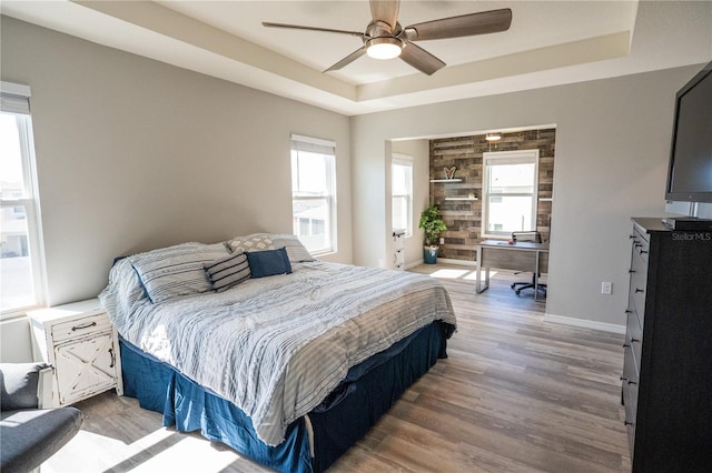 bedroom featuring a raised ceiling, ceiling fan, baseboards, and wood finished floors