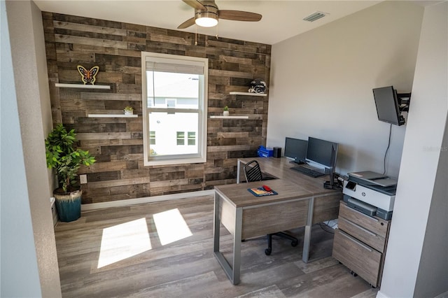 office area with a ceiling fan, visible vents, wooden walls, and wood finished floors