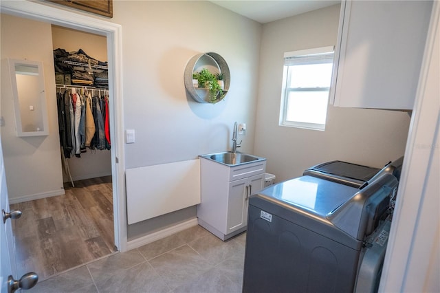 clothes washing area featuring a sink, washing machine and dryer, cabinet space, light tile patterned floors, and baseboards