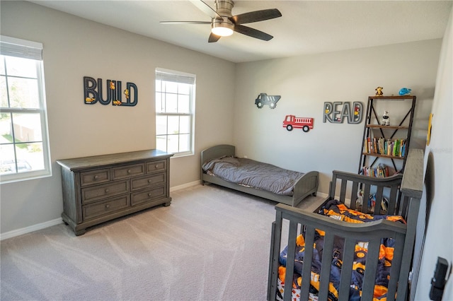 bedroom with a ceiling fan, light carpet, baseboards, and multiple windows