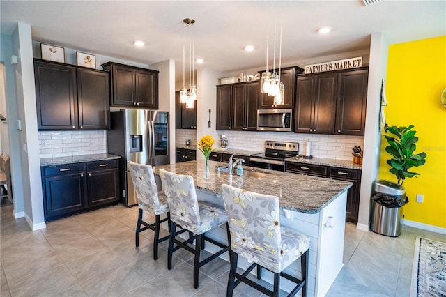 kitchen featuring stone countertops, a sink, stainless steel appliances, dark brown cabinets, and a kitchen breakfast bar