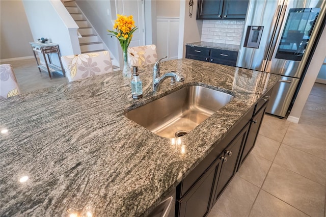 kitchen with dark stone countertops, stainless steel fridge, tasteful backsplash, and a sink