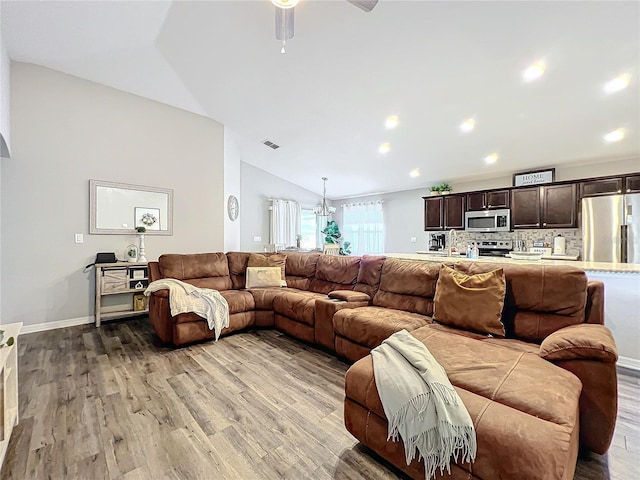 living room featuring lofted ceiling, light wood-type flooring, and ceiling fan with notable chandelier