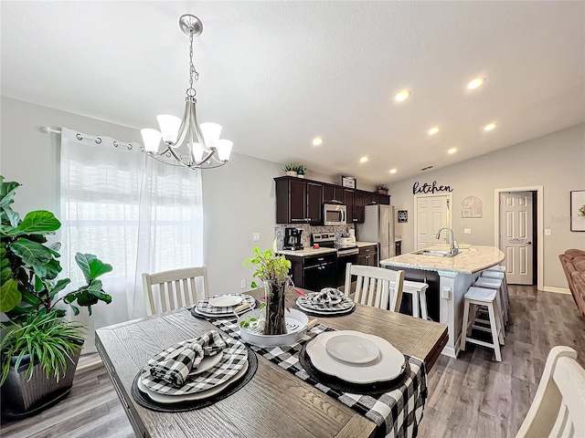 dining area featuring lofted ceiling, sink, a notable chandelier, and wood-type flooring