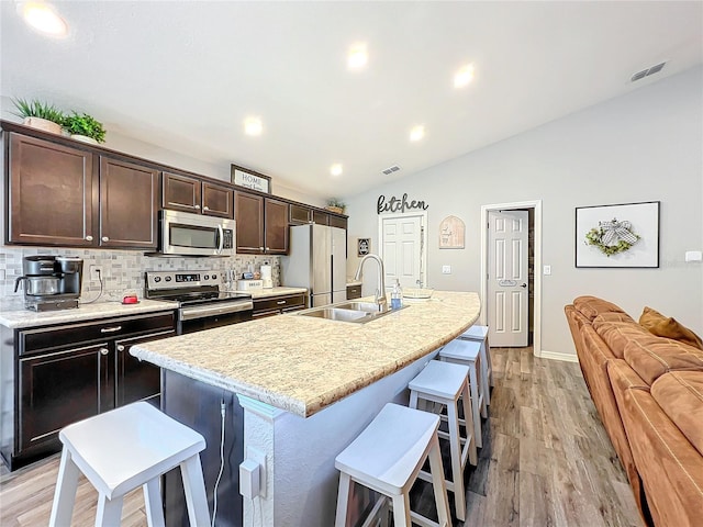 kitchen with sink, stainless steel appliances, lofted ceiling, light hardwood / wood-style flooring, and a kitchen island with sink