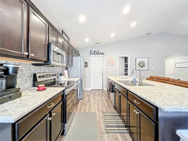 kitchen with a center island with sink, sink, vaulted ceiling, light wood-type flooring, and appliances with stainless steel finishes