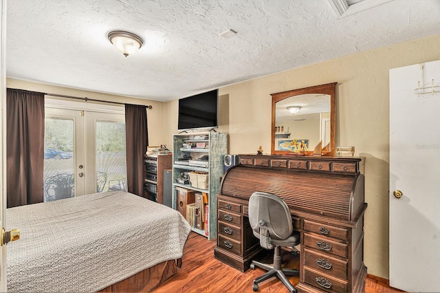 bedroom with access to exterior, hardwood / wood-style floors, a textured ceiling, and french doors