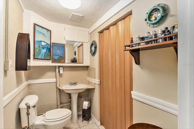 bathroom with tile patterned flooring, a textured ceiling, toilet, and sink