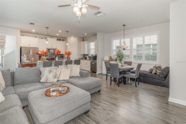 living room with wood-type flooring, ceiling fan with notable chandelier, and a textured ceiling