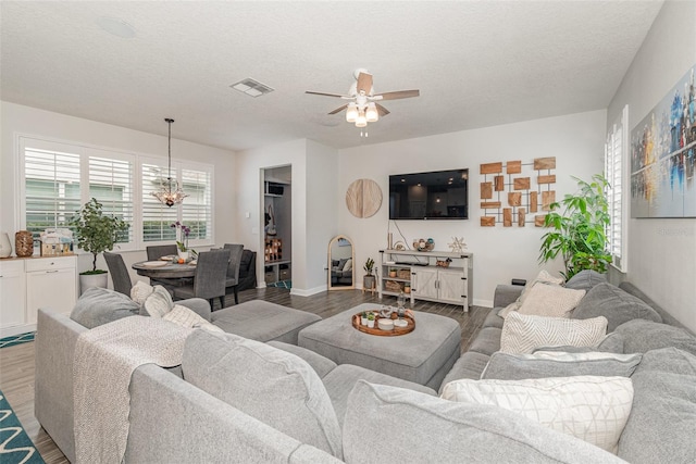 living room with hardwood / wood-style flooring, ceiling fan with notable chandelier, and a textured ceiling