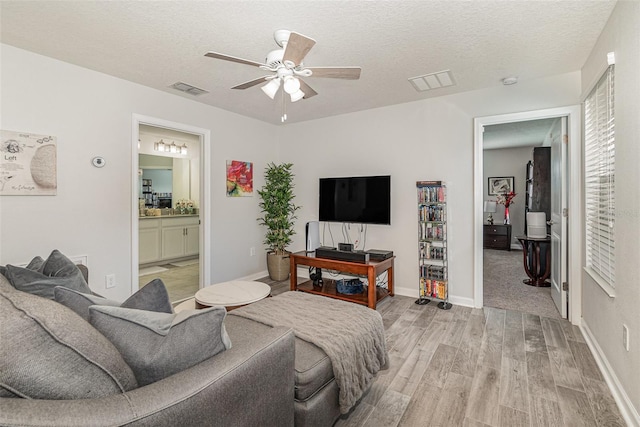 bedroom featuring a textured ceiling, light wood-type flooring, ensuite bathroom, and ceiling fan