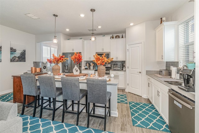 kitchen featuring tasteful backsplash, stainless steel appliances, decorative light fixtures, a center island, and white cabinetry