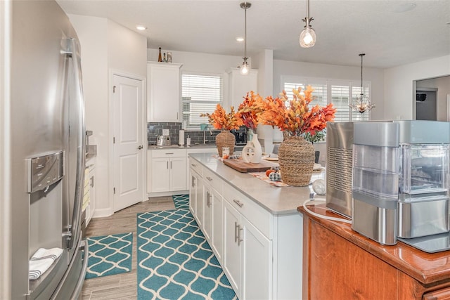 kitchen with stainless steel fridge, tasteful backsplash, pendant lighting, hardwood / wood-style floors, and white cabinetry