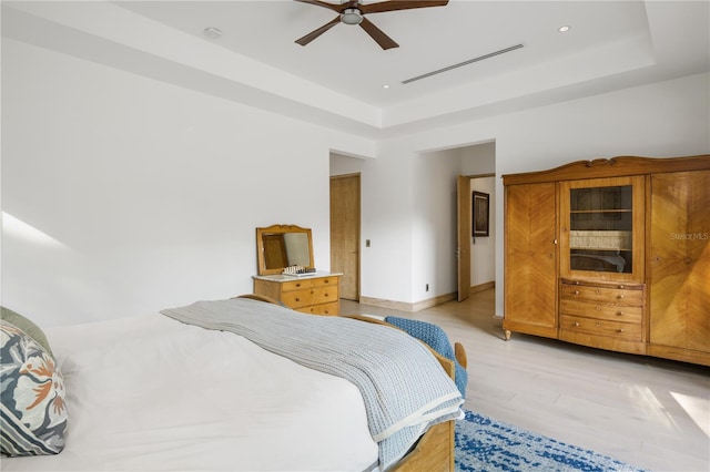 bedroom featuring light hardwood / wood-style floors, a raised ceiling, and ceiling fan