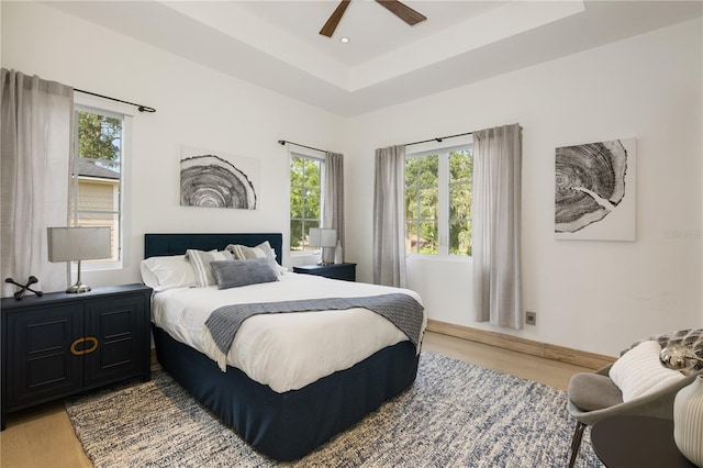 bedroom with a tray ceiling, multiple windows, light hardwood / wood-style floors, and ceiling fan