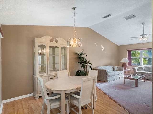 dining space featuring a textured ceiling, lofted ceiling, light wood-type flooring, and ceiling fan with notable chandelier