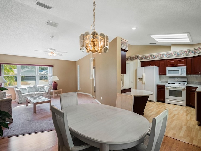 dining area with a textured ceiling, vaulted ceiling, light wood-type flooring, and ceiling fan with notable chandelier