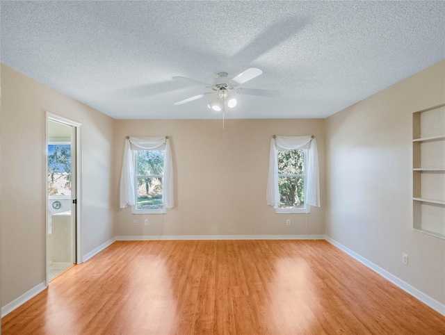 empty room with light hardwood / wood-style floors, a textured ceiling, ceiling fan, and built in shelves